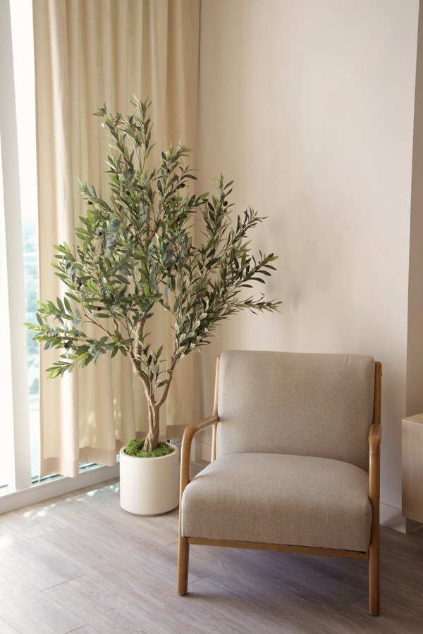 A faux olive tree filling a corner beside an accent chair